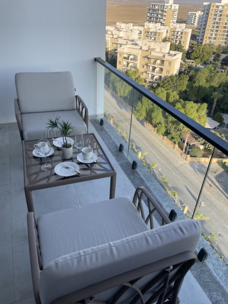 Balkon mit zwei Sesseln und einem Tisch, dekoriert mit Geschirr und Pflanzen.