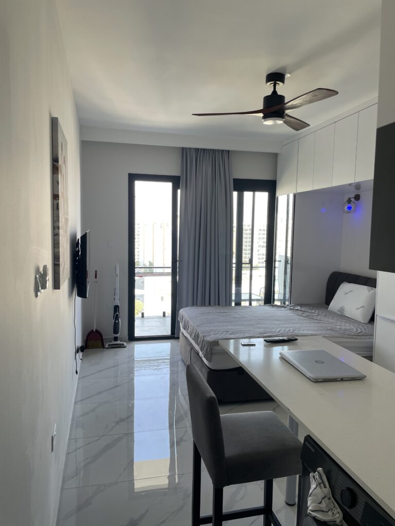 Kleine, helle Wohnung mit Bett, Tisch und Fernseher sowie Fenstern zur Terrasse.