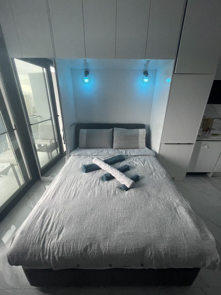 Doppelbett im modernen Schlafzimmer mit blauen Leuchten und Balkonzugang.
