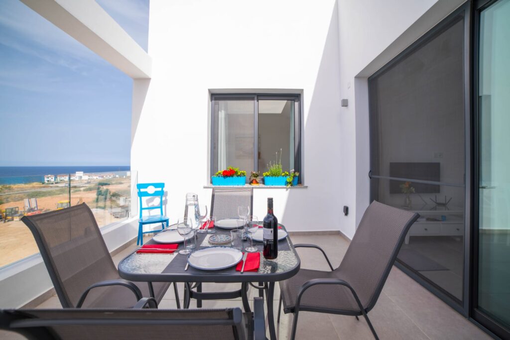 Essbereich auf der Terrasse mit Tisch, Stühlen, Weinflasche und Blick aufs Meer.