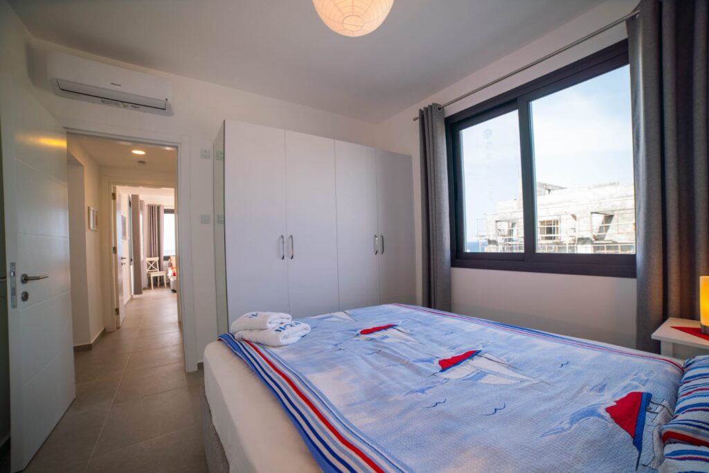 Schlafzimmer mit einem Bett, Schrank, Fenster und Flur im Hintergrund.