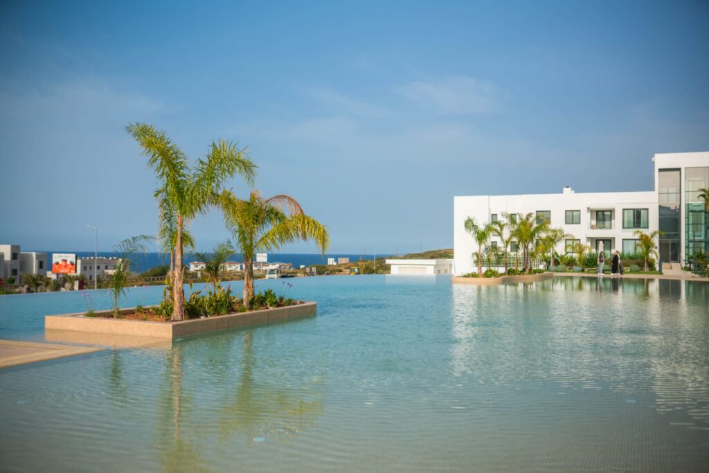 Poollandschaft mit Palmen und modernem Gebäude am Wasser.