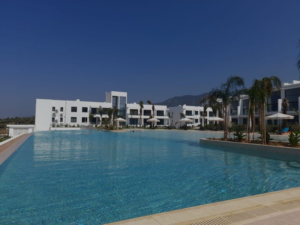 Poollandschaft mit modernen Gebäuden und Palmen unter blauem Himmel.