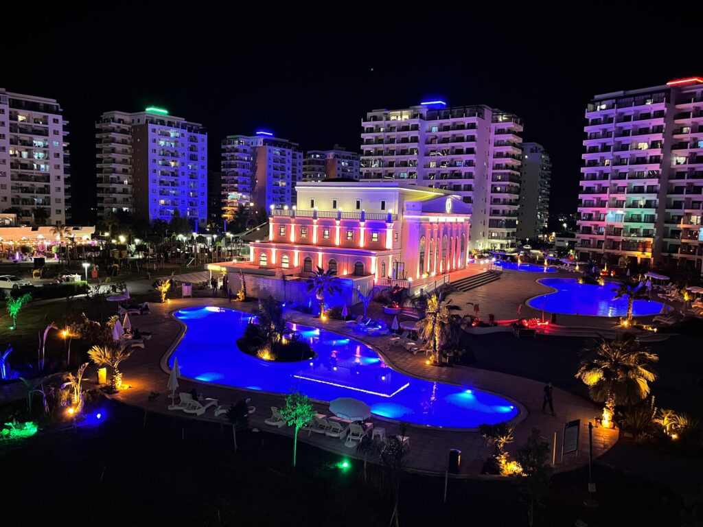 Illuminierte Hotelanlage mit mehreren Gebäuden und beleuchtetem Pool bei Nacht.