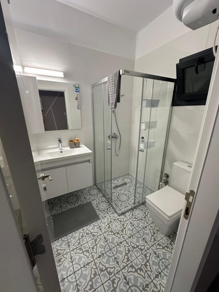 Badezimmer mit Glasdusche, WC und modernen Fliesenboden.