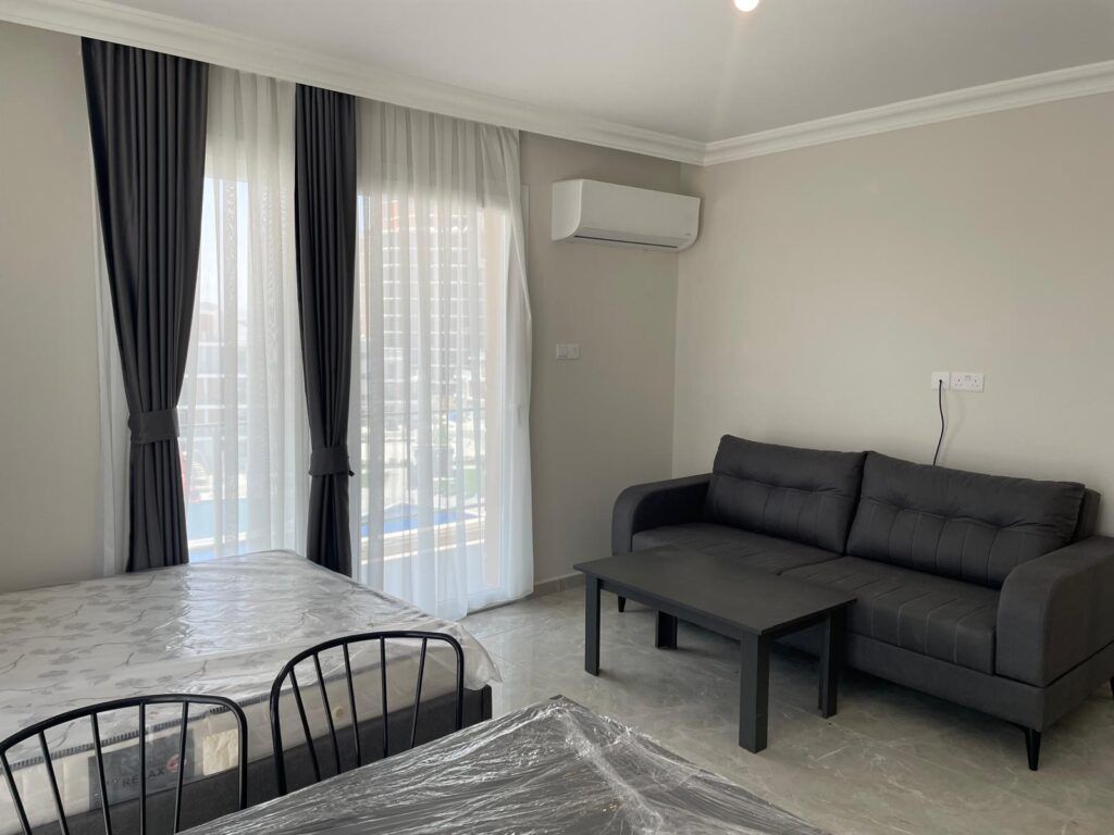 Wohnzimmer mit grauem Sofa, Tisch und Blick auf Fenster mit Vorhängen.