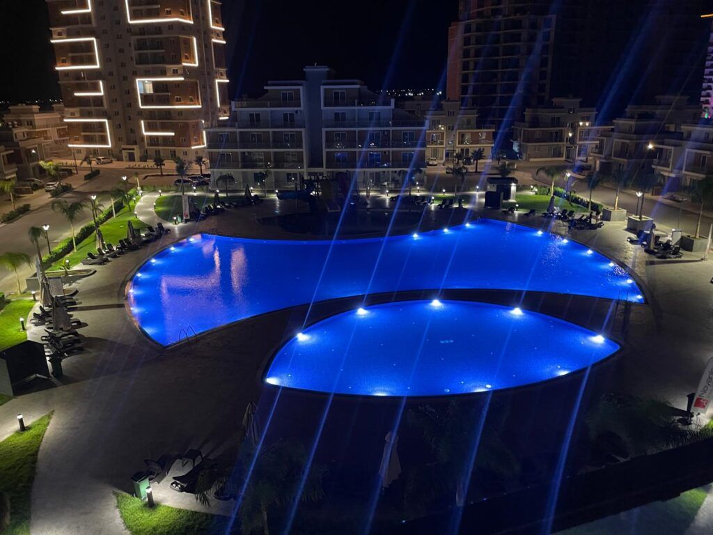 Beleuchteter Poolbereich mit zwei großen, blauen Wasserflächen bei Nacht.