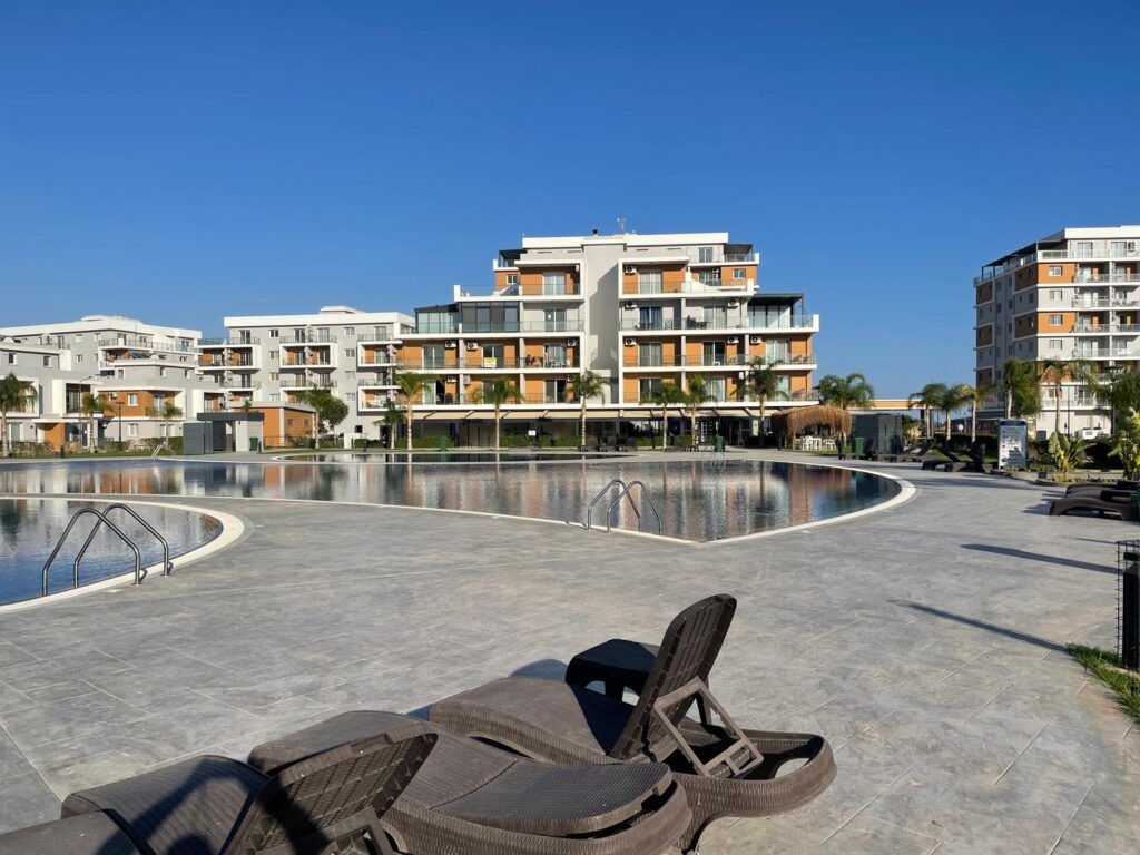 Moderne Wohnanlage mit Pool, Liegen und klar blauem Himmel im Hintergrund.
