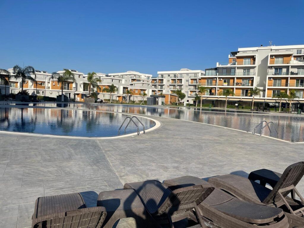 Poolbereich mit Liegen und modernen Gebäuden im Hintergrund.