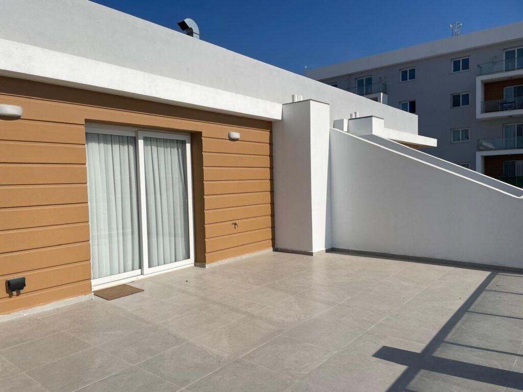 Terrasse mit Fliesen und Glastür, umgeben von weißen und braunen Wänden.